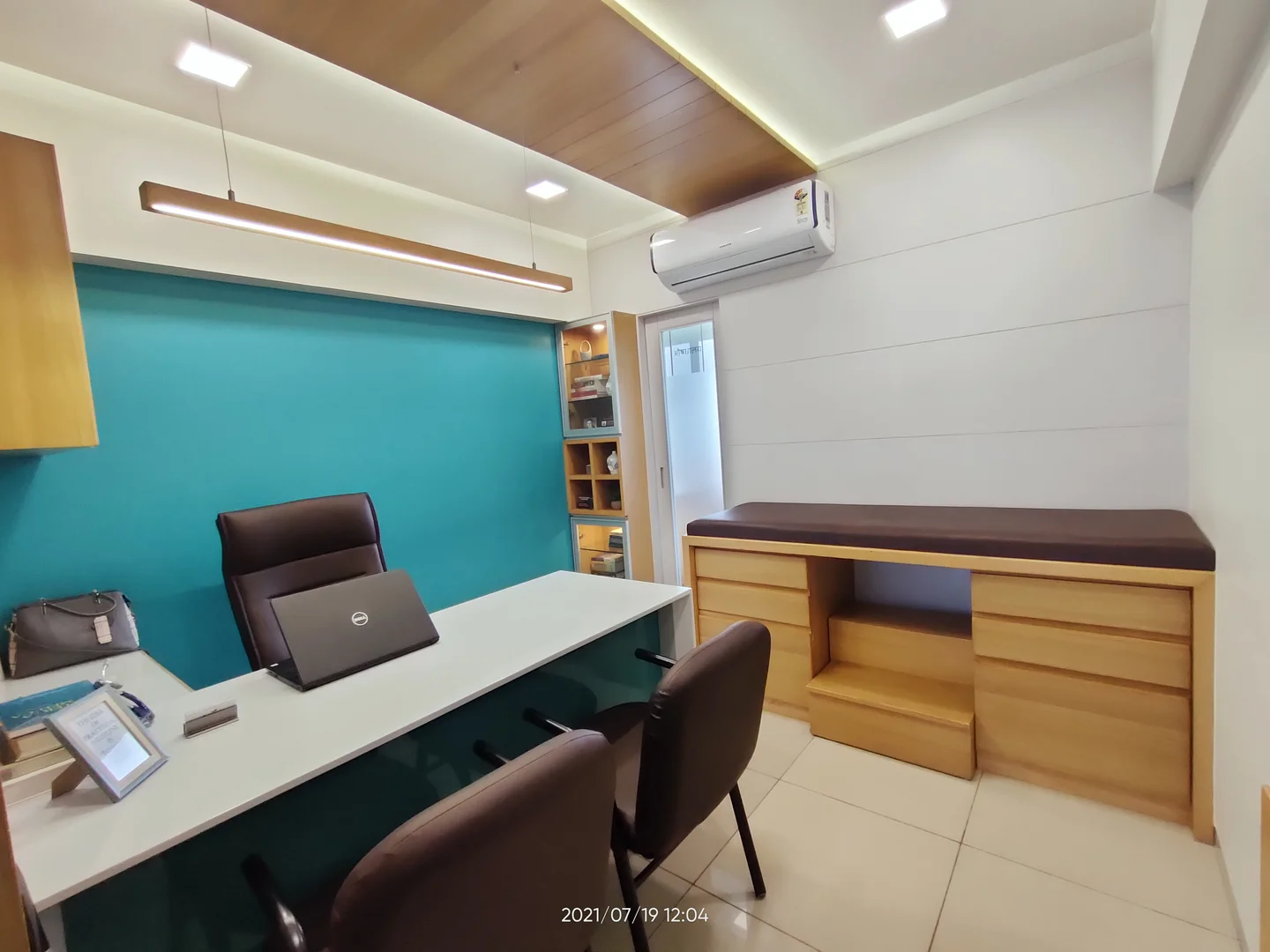 The consulting room at Aayat: a white desk against the full turquoise wall, with the examination bench opposite